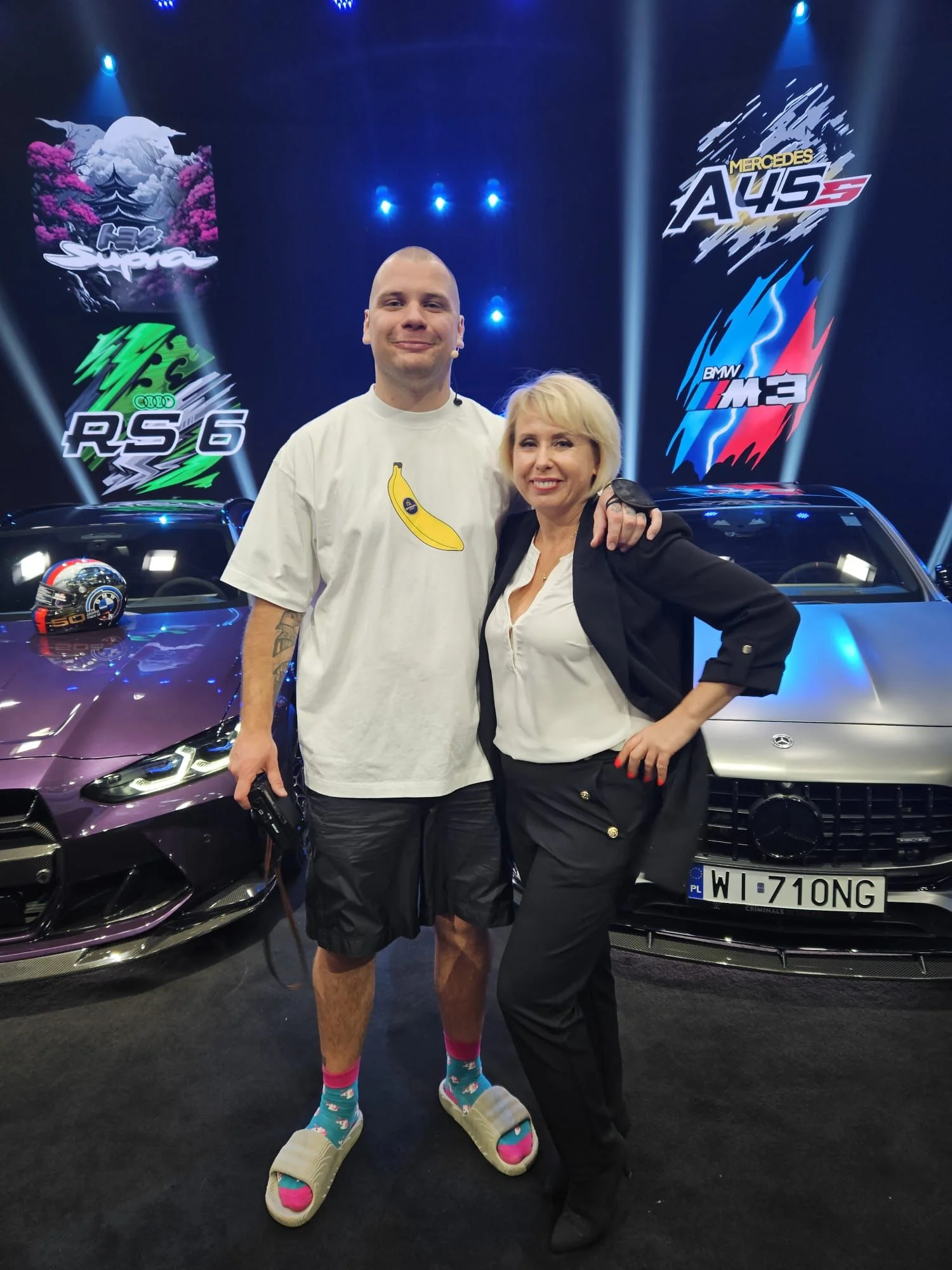Beata Wentura-Dudek z Buddą podczas losowania loterii - w tle BMW M3, Mercedes-AMG A45S oraz Audi RS6 i Toyota Supra