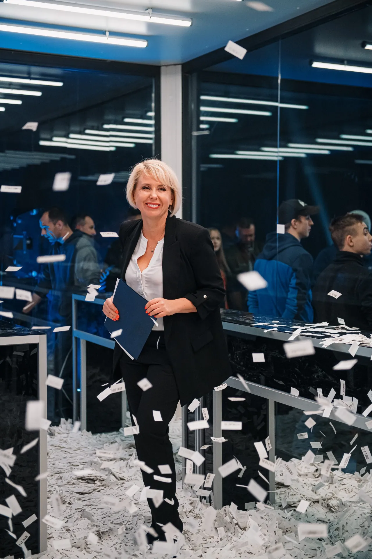 Beata Wentura-Dudek z niebieską teczką - dokumentacja w trakcie losowania loterii, w tle uczestnicy